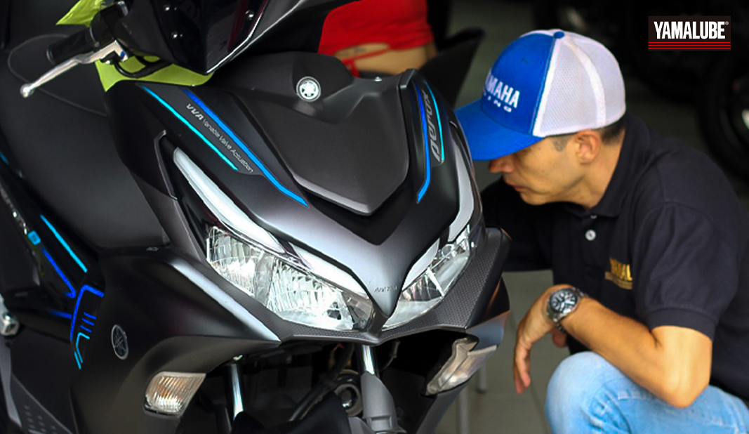 Técnico aplicando productos Yamalube en una motocicleta Yamaha Aerox 155 durante una sesión de mantenimiento.
